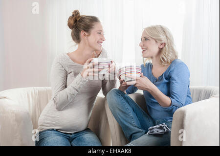 Due donne tee potabile parlando sedia a casa Foto Stock