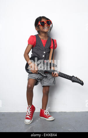 Ragazza con chitarra giocattolo indossando cuore rosso a forma di occhiali da sole Foto Stock