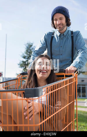 Giovane uomo giovane divertimento spingendo carrello della spesa Foto Stock