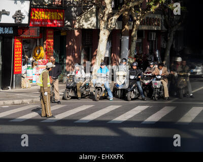 Il popolo cinese su scooter in attesa per la polizia l'uomo a far loro attraverso, Shanghai, Cina Foto Stock