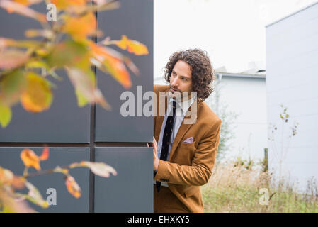 Abito uomo guarda sospettoso nosy nascondendo a parete Foto Stock