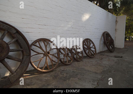 In legno antico le ruote del carro puntellato contro un muro dipinto di bianco in un pittoresco South African casale in Montagu, Western Cape. Foto Stock