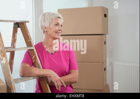 Senior woman standing con scaletta in appartamento nuovo, Baviera, Germania Foto Stock