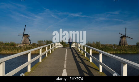 L'uomo attraversando a piedi ponte sull'acqua a Kinderdijk nei Paesi Bassi, famosa per i suoi numerosi mulini a vento. Foto Stock