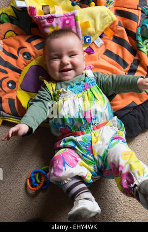 8 mese fa Baby girl, sdraiato sul pavimento ridendo Foto Stock