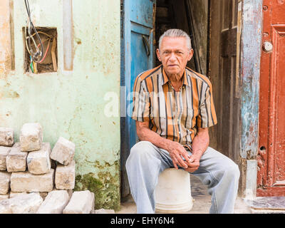 Un ispanico senior citizen poggia come egli siede sulla parte anteriore stoop della sua casa a Santiago de Cuba. Foto Stock