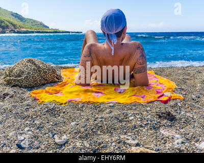 Un giovane maschio tatuato sunbather giace sul suo telo mare in spiaggia in Siboney, Cuba. Foto Stock