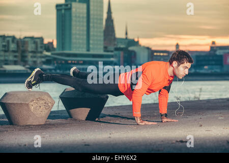 Runner maschio facendo push-up contro la skyline della città Foto Stock