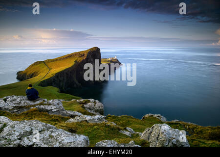 Metà uomo adulto seduto su una roccia che guarda al mare a Neist Point, Scozia Foto Stock