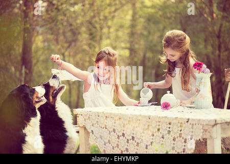 Due ragazze avente un tea party in giardino con due cani Foto Stock