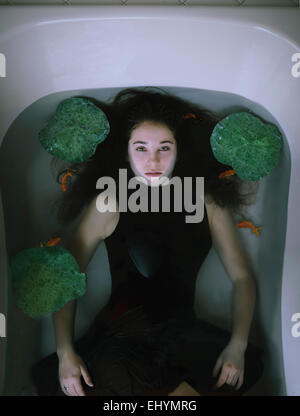 Vista aerea di una giovane donna giaceva in una vasca con pesci rossi e ninfee Foto Stock