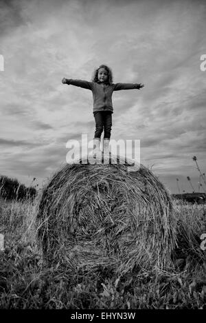 Ragazza in piedi su una balla di fieno in un campo, Polonia Foto Stock