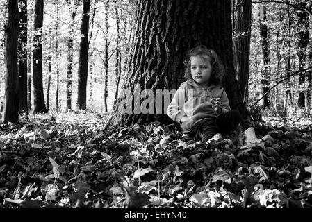 Ragazza seduta nei boschi appoggiata contro un tronco d'albero, Polonia Foto Stock