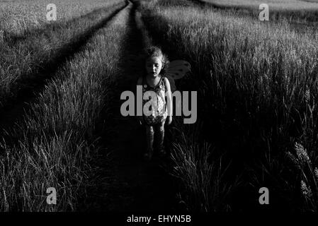 Ragazza che indossa le ali di fata in piedi in un campo di grano in estate, Polonia Foto Stock