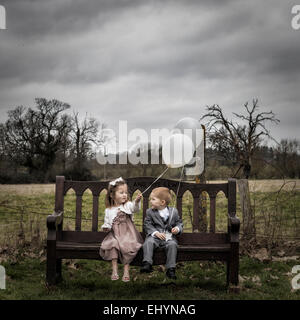 Ragazzo e una ragazza seduta su una panchina con palloncini Foto Stock
