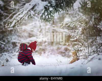 Baby boy giocare nella neve con un orsacchiotto di peluche Foto Stock