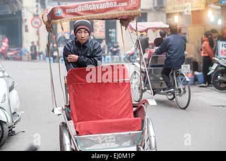 In rickshaw driver attende i clienti nel quartiere vecchio di Hanoi, Vietnam. Foto Stock