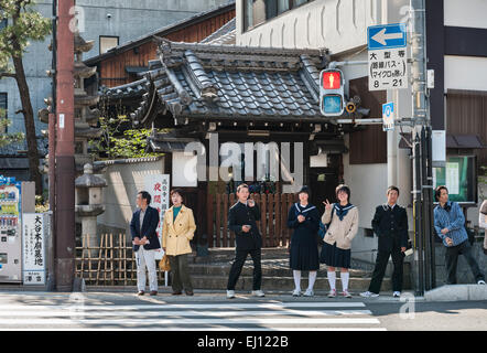 Kyoto, Giappone. In attesa di attraversare la strada, una ragazza in uniforme scolastica flicks un segno di pace Foto Stock