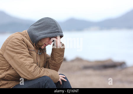 Preoccupati di adolescente Guy piange sulla spiaggia in inverno in un cattivo tempo giorno Foto Stock