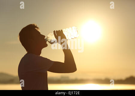 Profilo di un fitness silhouette uomo acqua potabile da una bottiglia al tramonto con il sole in background Foto Stock