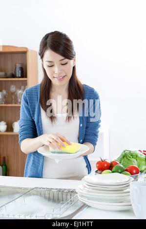 Giovane donna piastre di lavaggio nel lavello da cucina con sorriso, Foto Stock
