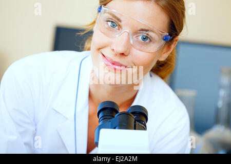 Bella donna in un laboratorio lavora con un microscopio. Foto Stock