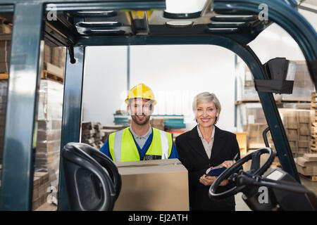 Responsabile magazzino sorridente in telecamera con driver di carrello elevatore a forche Foto Stock