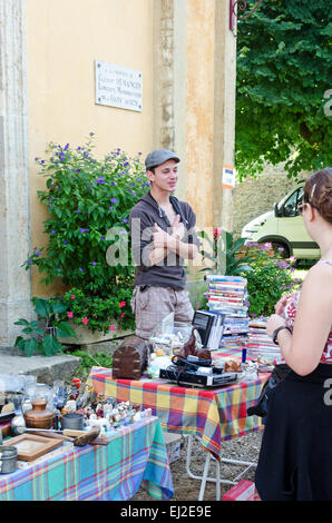 Un giovane uomo di chat con i clienti presso il villaggio marché aux puces in Gigny-sûr-Saône, Borgogna. Foto Stock