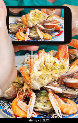 Fotografare il concetto di cibo - tourist prende immagine della piastra con il granchio tagliato, ostriche, gamberetti e altri frutti di mare sullo smartphone, Fra Foto Stock