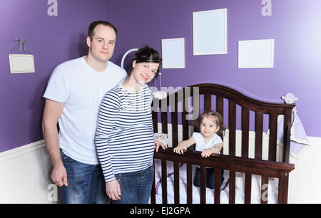 Famiglia all'interno della stanza del bambino con il bambino nel presepe. Foto Stock