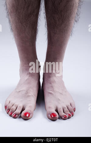 Uomo di piedi con il rosso smalto per unghie e gambe pelose luminoso su sfondo grigio Foto Stock