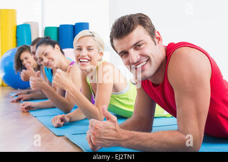 Amici gesticolando Thumbs up sdraiati su stuoie in palestra Foto Stock