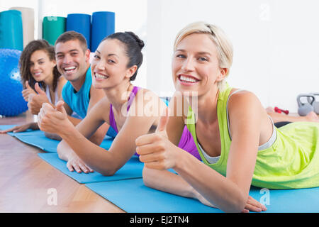 Amici gesticolando Thumbs up sdraiati su stuoie in palestra Foto Stock