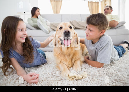 I fratelli stroking cane sul tappeto mentre i genitori rilassarsi sul divano Foto Stock