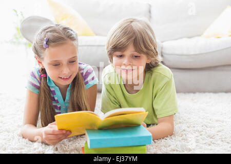 I fratelli la lettura di libro mentre giacenti su rug Foto Stock