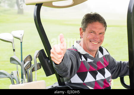 Felice golfista alla guida della sua golf buggy sorridente in telecamera Foto Stock