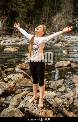 9 anno vecchia ragazza con entusiasmo e con gioia gettando le braccia fuori ampia, nel fiume Snoqualmie in North Bend, Washington Foto Stock