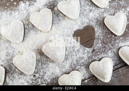 Ravioli di greggio in forma di cuori, cospargere di farina, scuro su un tavolo di legno. Gnocchi di cottura. Vista dall'alto. Foto Stock