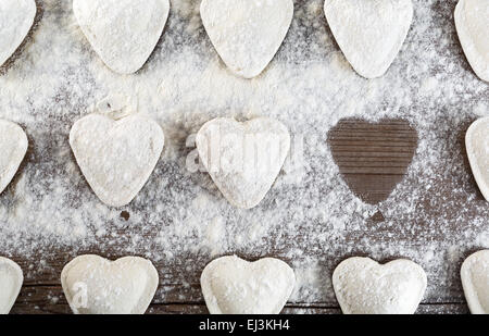 Gnocchi di cottura. Ravioli di greggio in forma di cuori, cospargere di farina, su sfondo di legno closeup. Vista dall'alto. Foto Stock