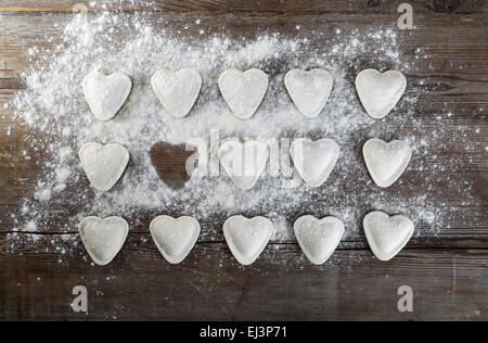 Ravioli di greggio in forma di cuori, cospargere di farina, sul legno scuro dello sfondo. Gnocchi di cottura. Vista dall'alto. Foto Stock