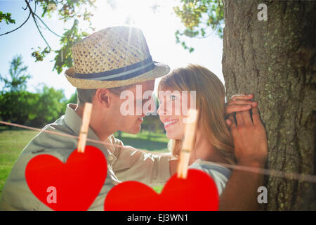 Immagine composita di carino coppia sorridente appoggiata contro la struttura ad albero nel parco Foto Stock