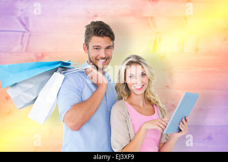 Immagine composita di attraente coppia giovane azienda shopping bags utilizzando tablet pc Foto Stock