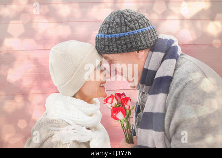 Immagine composita di felice coppia matura in abbigliamento invernale con rose Foto Stock