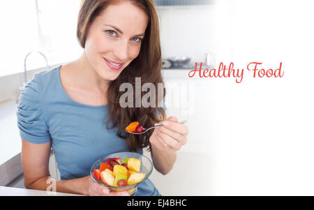 Cibo sano contro sorridente giovane donna di mangiare insalata di frutta in cucina Foto Stock