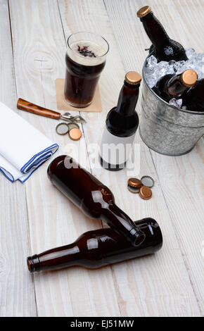 Alta angolazione di un partito benna riempita con bottiglie di birra su una tavola in legno rustico. Le bottiglie vuote e i tappi di bottiglia sono sul tabl Foto Stock