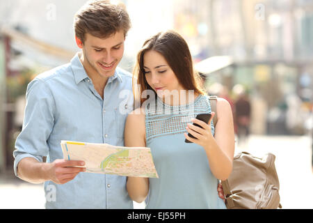 Coppia di turisti consultando la guida di una città e il telefono cellulare gps in una strada Foto Stock