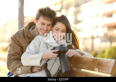 Coppia di turisti rivedendo le foto di una fotocamera reflex digitale seduto su una panchina di un parco con un background urbano Foto Stock