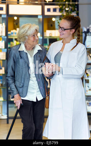 Femmina giovane farmacista tenendo delicatamente e senior di supporto paziente di sesso femminile in farmacia. Foto Stock