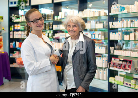 Signora senior con un bel sorriso si stringono la mano con un bel giovane farmacista femmina come stanno insieme nella farmacia discu Foto Stock