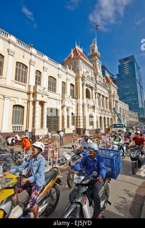 La popolazione locale sulla moto in movimento nella parte anteriore del popolo del comitato dell edificio. La città di Ho Chi Minh, Vietnam. Foto Stock